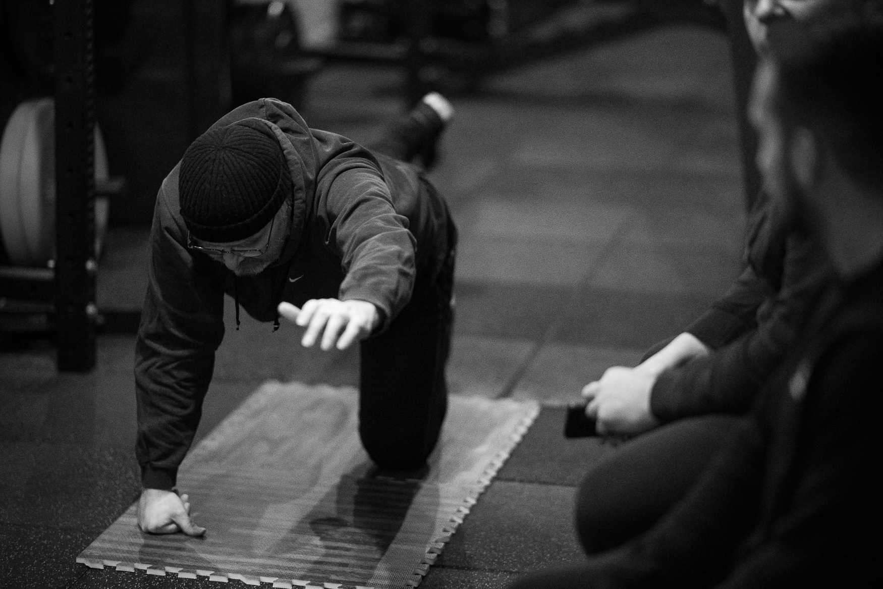 A coach kneeling beside a member, guiding them through a bird-dog on the studio floor.